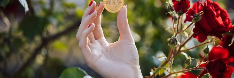 mano sujetando moneda con logo bitcoin con unas rosas en el fondo.