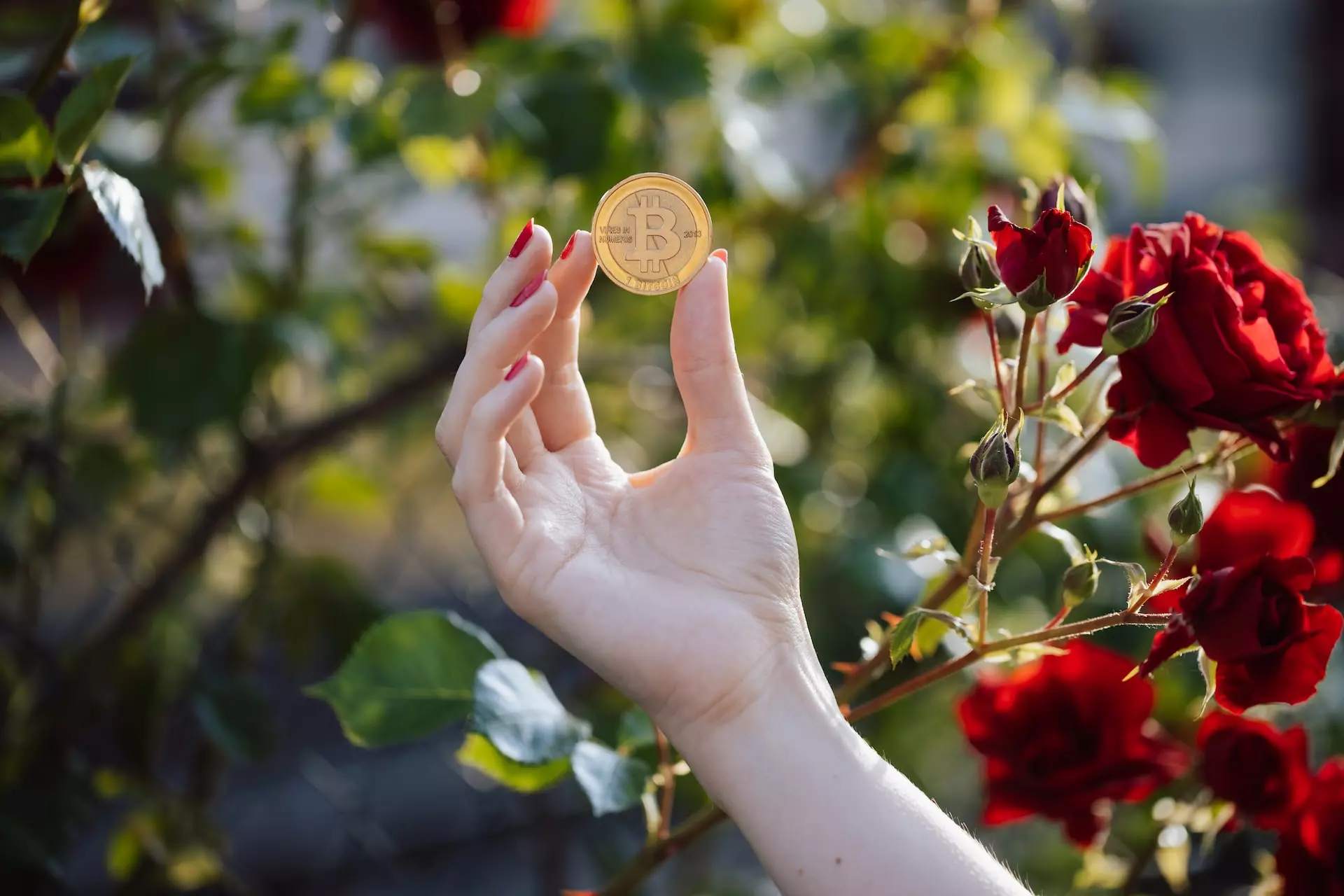 mano sujetando moneda con logo bitcoin con unas rosas en el fondo.
